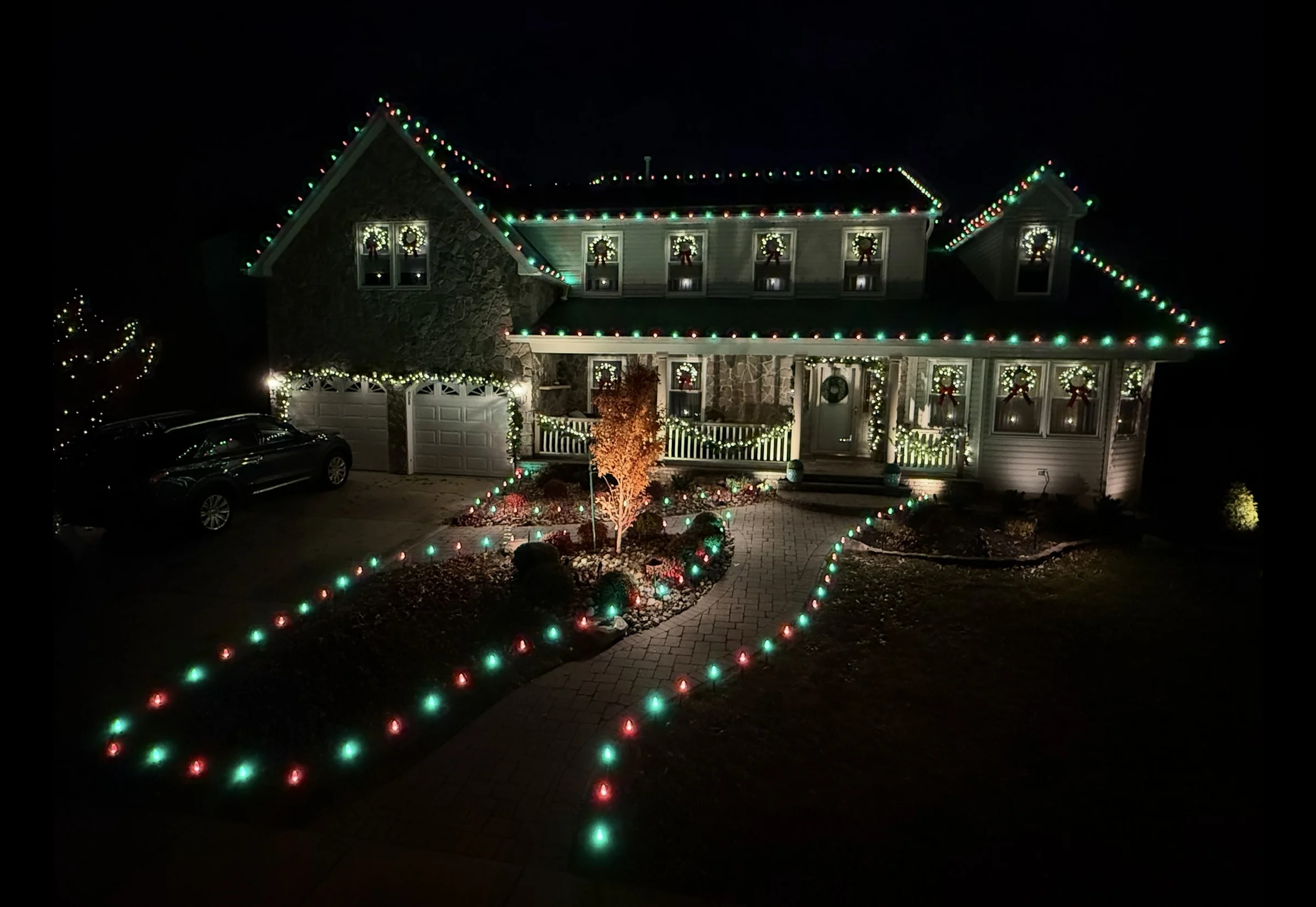 Red and green roofline lights, window wreaths, and illuminated garden paths on a two-story home