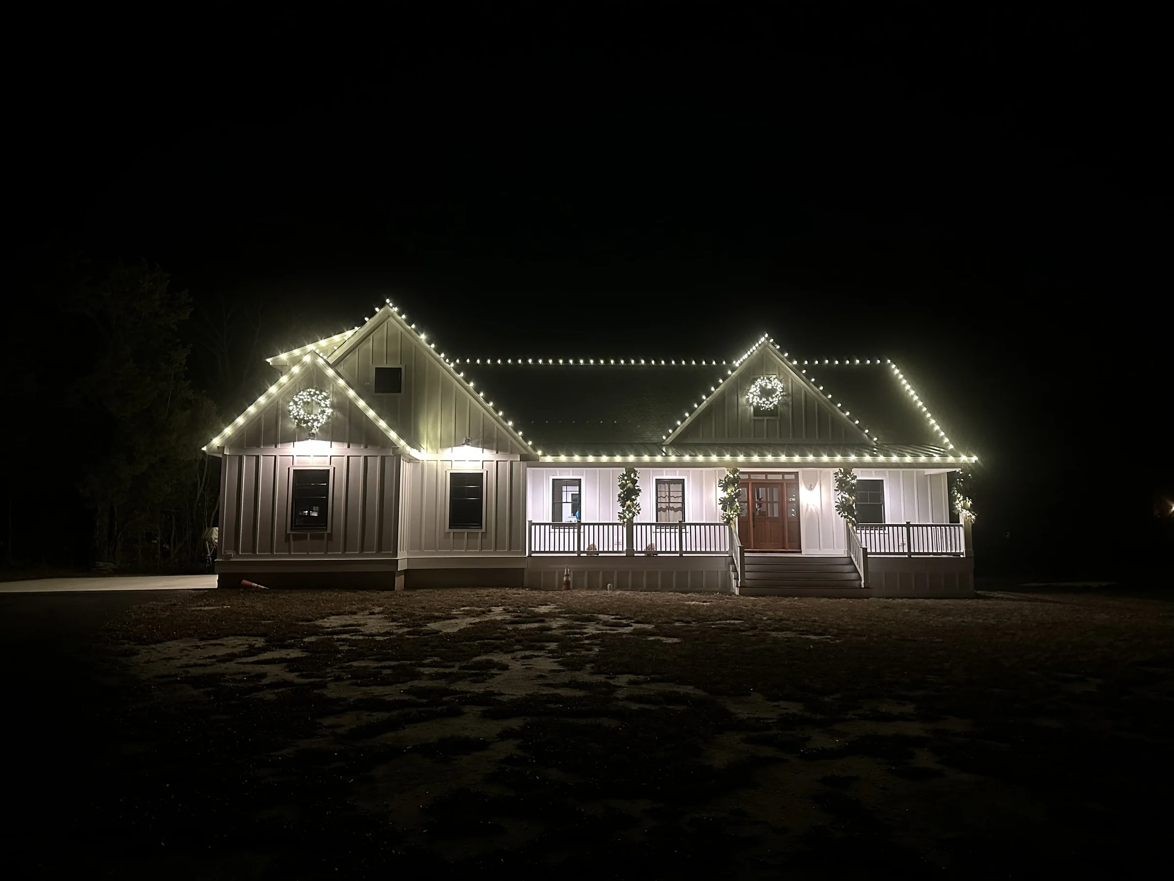 Warm white Christmas lights outlining roof peaks with wreaths and garland across the front porch