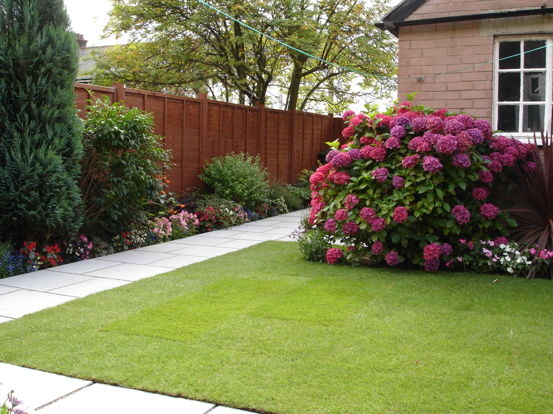 Fresh green sod lawn with stone garden path and colorful flower borders